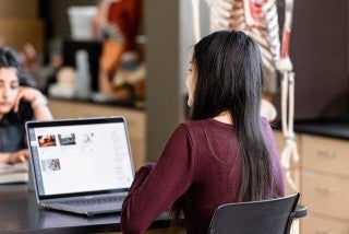 two girls study together on laptops in a lab